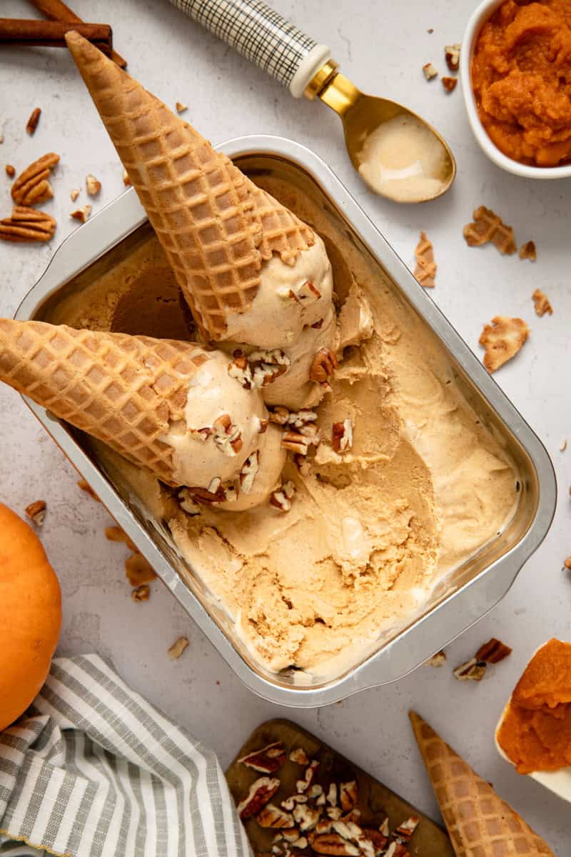 Pumpkin ice cream in a couple of cones laying in a tray of ice cream.