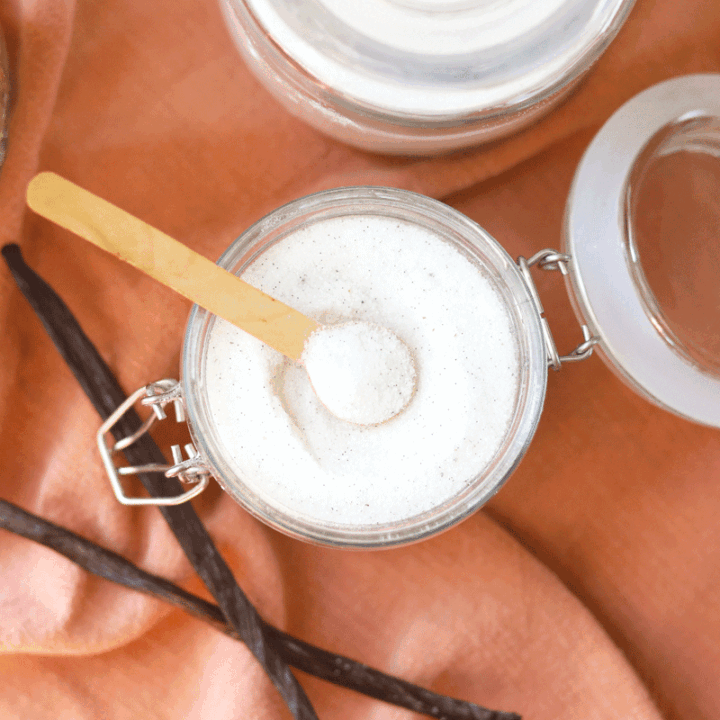 a jar of sugar with vanilla beans in it and sugar and vanilla laying next to it on a table