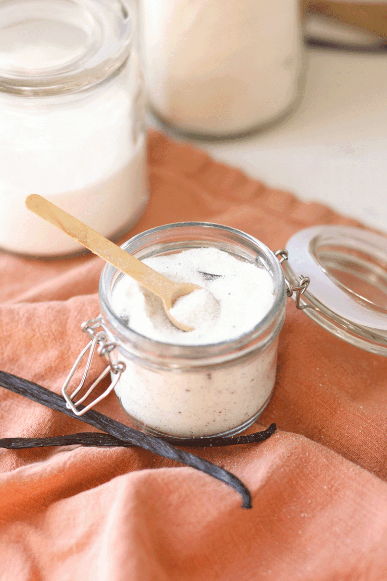 a jar of sugar with vanilla beans in it and sugar and vanilla laying next to it on a table