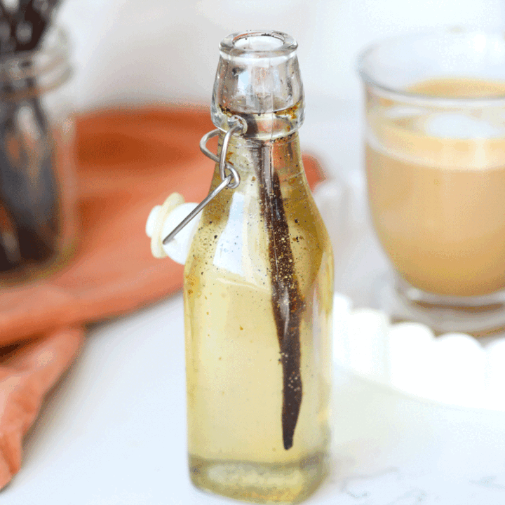 A glass bottle of vanilla syrup with a whole fresh vanilla bean in it