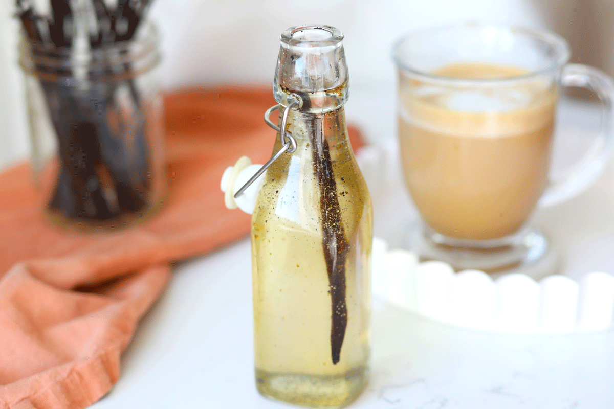 A glass bottle of vanilla syrup with a whole fresh vanilla bean in it