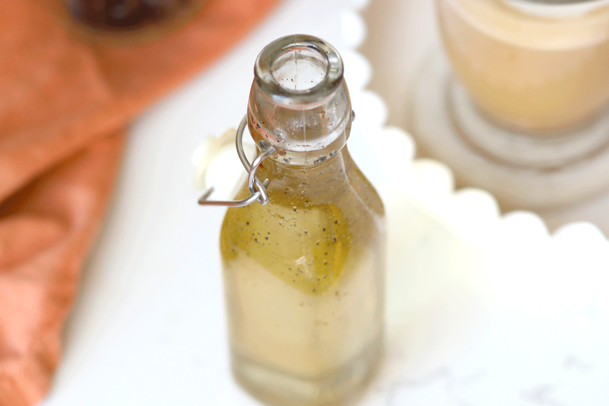 A glass bottle of vanilla syrup with a whole fresh vanilla bean in it