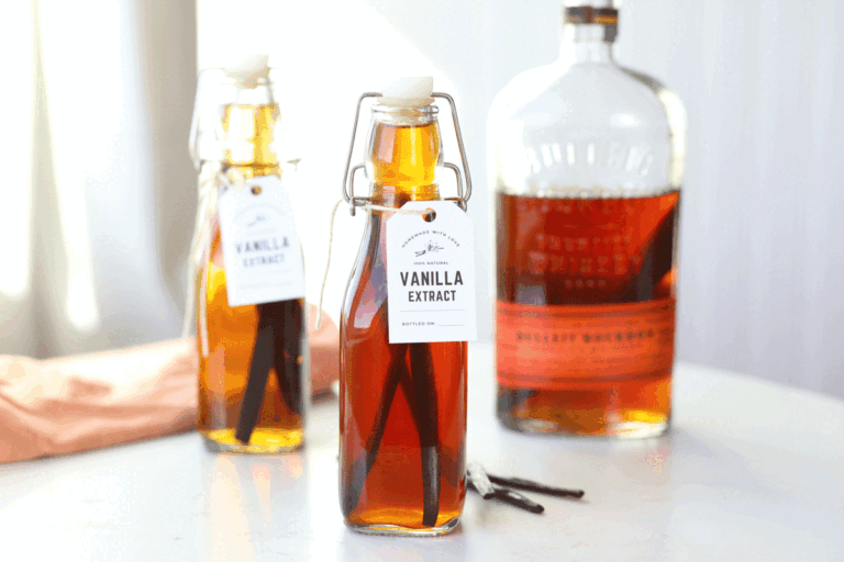 Homemade vanilla extract with a bottle of bourbon in the background and vanilla beans in the foreground