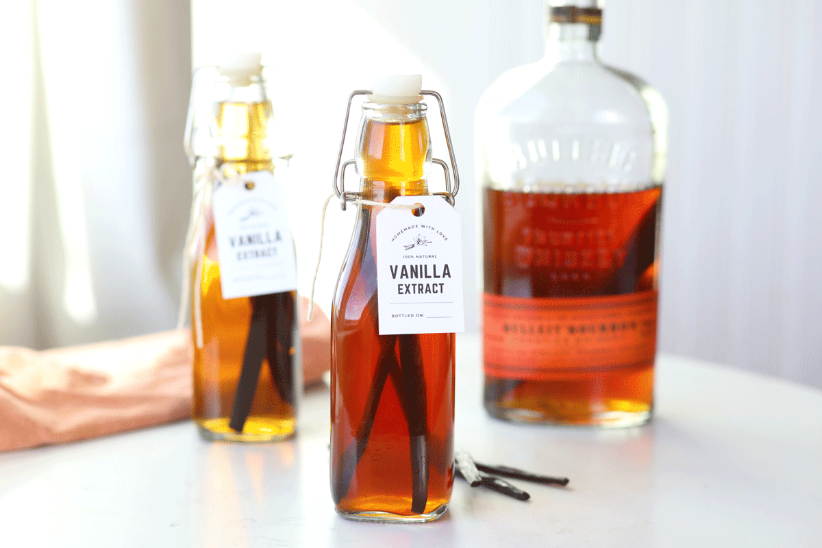 Homemade vanilla extract with a bottle of bourbon in the background and vanilla beans in the foreground