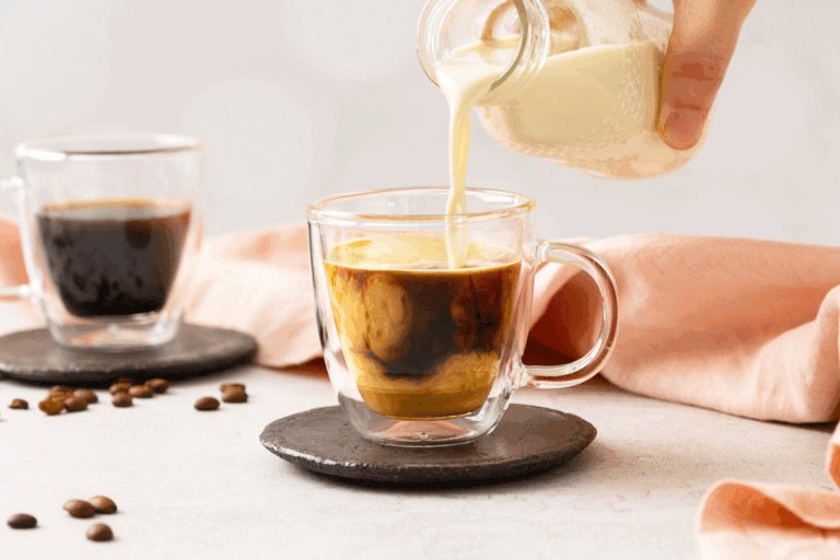 Homemade coffee creamer being poured from a glass bottle into a hot cup of coffee.