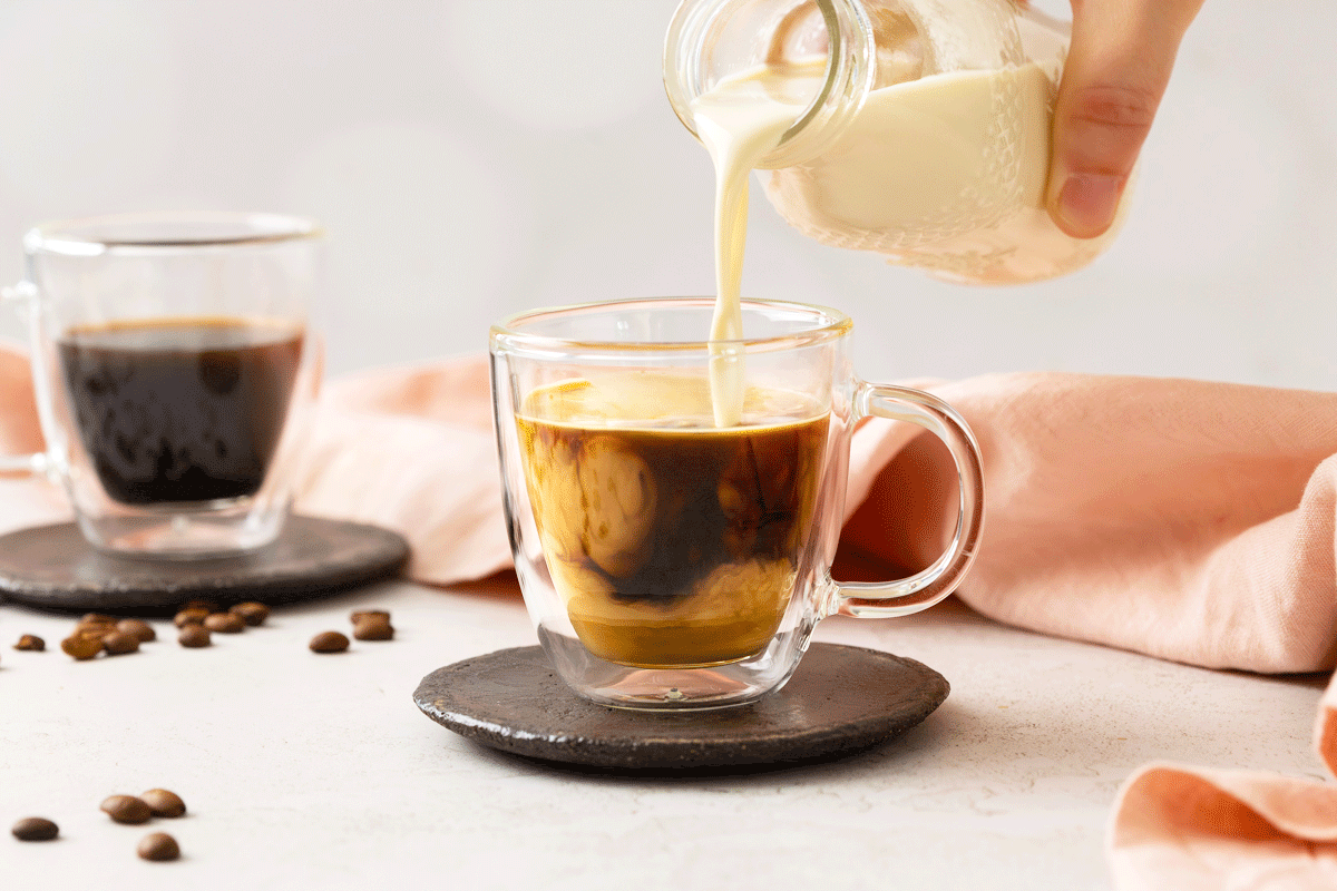 Homemade coffee creamer being poured from a glass bottle into a hot cup of coffee.
