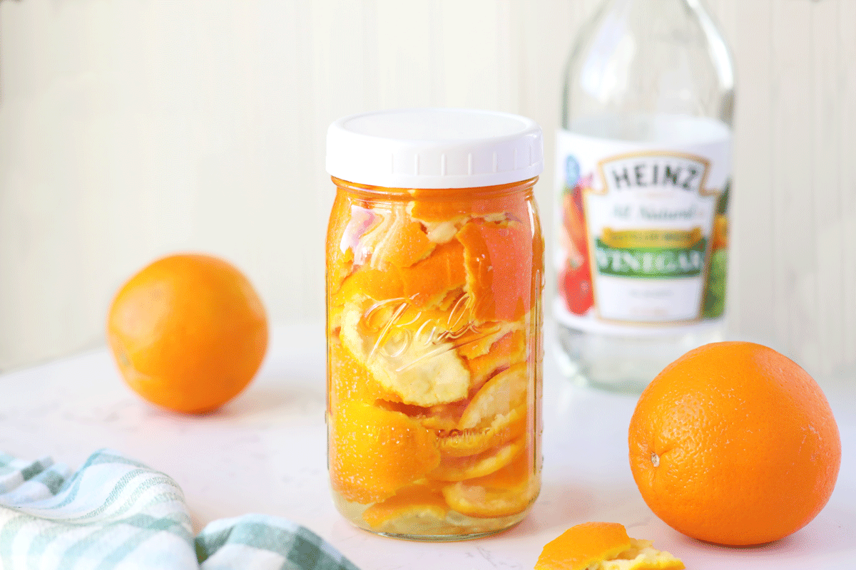 A mason jar of orange peels with white vinegar in the background.