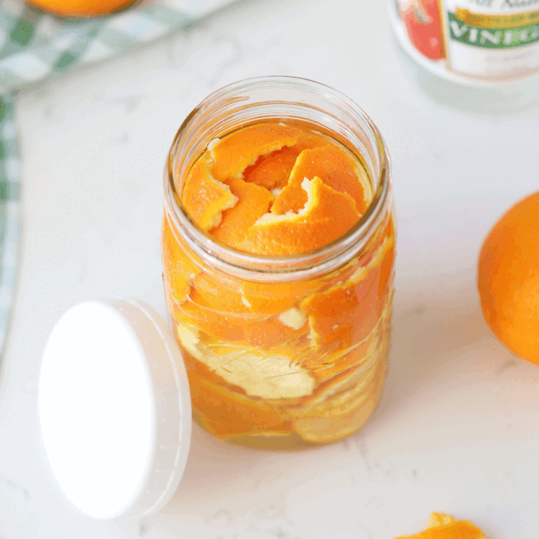 A mason jar of orange peels with white vinegar in the background.