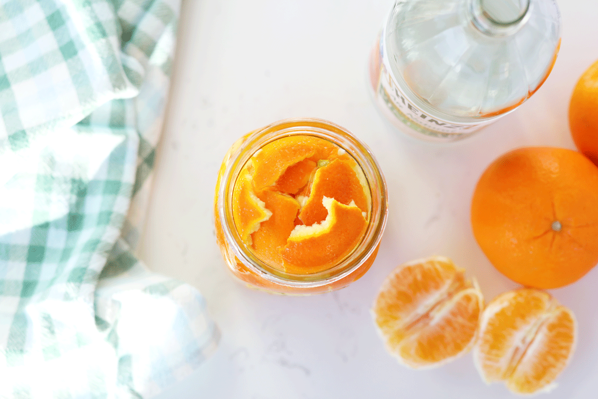 A mason jar of orange peels with white vinegar in the background.