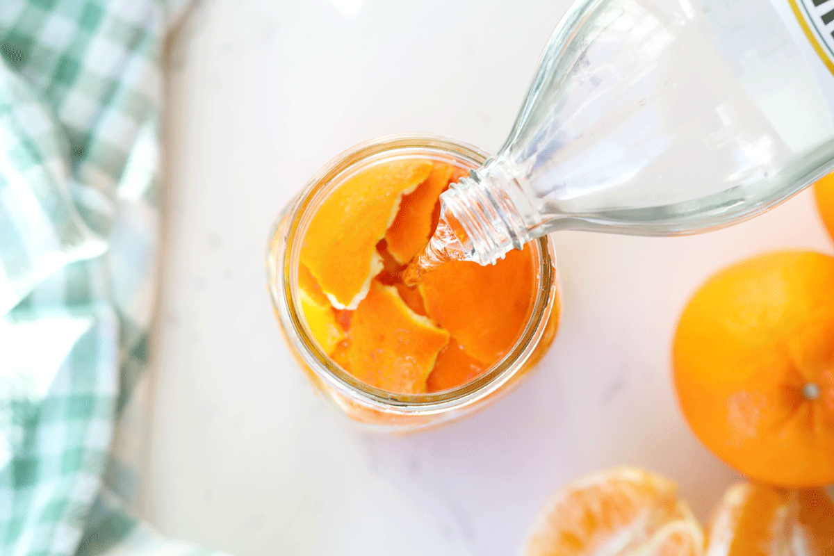 White vinegar being poured into a jar of orange peels